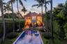 Spanish Colonial architecture featuring a crenellated tower, red tile roof, rectangular swimming pool, brick-paved patio, and mature palm trees