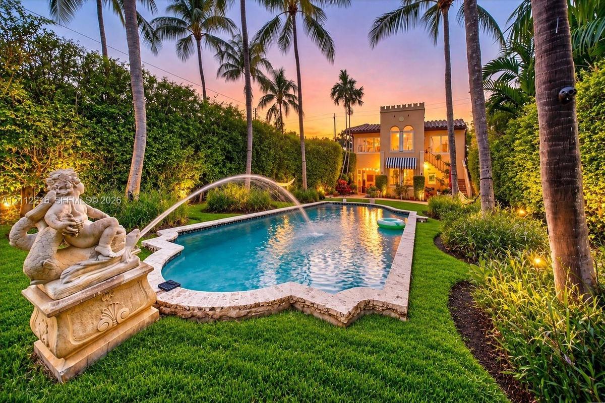 Resort-style backyard featuring a stone-trimmed swimming pool, integrated fountain, ornate sculpture, manicured lawn, and mature palm trees