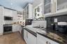 Kitchen featuring white cabinetry with glass-front uppers, apron-front farmhouse sink, stone countertops, stainless steel appliances, and patterned ti