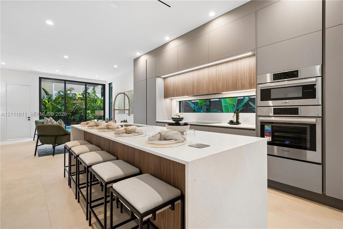 Modern kitchen featuring flat-panel cabinetry, a central island with a solid-surface countertop, integrated stainless steel double wall ovens, recesse