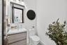Vanity with a rectangular basin, wood-finish cabinetry, wall-mounted mirror, three-light fixture, and dual-flush toilet