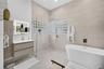 Bathroom featuring a freestanding soaking tub, walk-in shower with glass partition, neutral large-format wall tile, wood-finish wall-mounted vanity, a