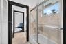 Full bathroom featuring a tub-shower combination with a sliding glass enclosure, large-format stone-finish wall and floor tiling, and dark-finished do