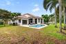 Stucco exterior featuring a clay tile roof, expansive concrete pool deck, in-ground swimming pool, and mature landscaping