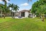 Expansive backyard featuring a concrete patio, swimming pool, mature palm trees, and floor-to-ceiling glass windows