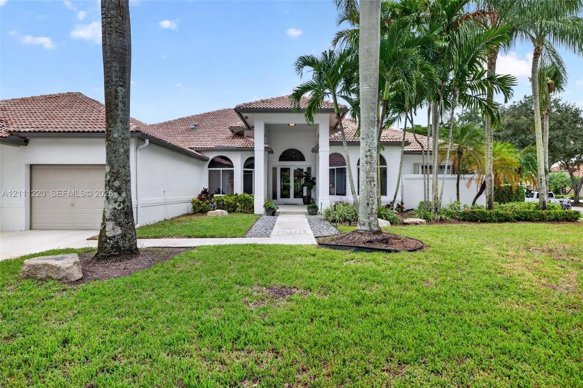 Stucco exterior featuring a tile roof, arched windows, covered entryway, and manicured landscaping with mature palm trees