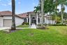 Stucco exterior featuring a tile roof, arched windows, covered entryway, and manicured landscaping with mature palm trees