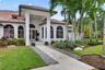 Mediterranean-style exterior featuring a covered entryway, stucco facade, arched windows, concrete walkway, and mature palm trees
