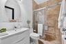 Contemporary white vanity with integrated basin, polished chrome faucet, circular wall mirror, and walk-in shower featuring floor-to-ceiling stone-loo