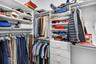 Walk-in closet featuring white built-in shelving, multi-level clothing rods, and a stack of four integrated storage drawers