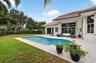 Rear exterior featuring a swimming pool, expansive concrete patio, manicured lawn, tile roof, and floor-to-ceiling glass doors