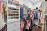 Walk-in closet featuring white built-in shelving, multiple pull-out drawers, tiered clothing rods, and dark-toned wood-finish flooring