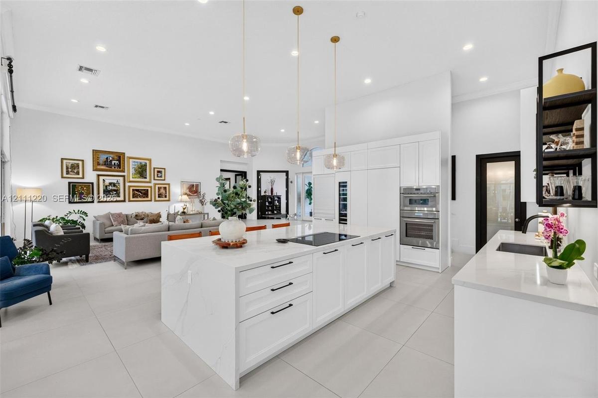 Kitchen featuring a large central island with quartz surfacing, white shaker-style cabinetry, stainless steel double wall ovens, three glass pendant l
