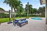 Backyard featuring a concrete patio, kidney-shaped swimming pool, manicured lawn, and mature palm trees enclosed by privacy hedging