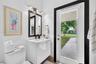 Modern floating vanity with a vessel sink, dark-framed vanity mirror, multi-bulb wall-mounted lighting, and an exterior glass door leading to a concre