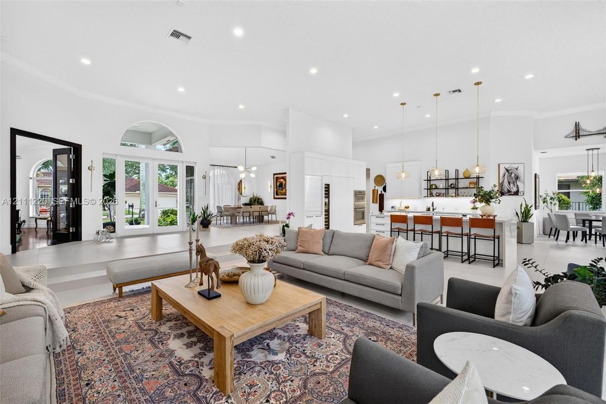 Open-concept interior featuring large-format tile flooring, recessed lighting, arched window accents, double glass-paned doors, and a kitchen island w