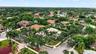 Aerial perspective of a corner lot residence featuring a tile roof, paved driveway, established perimeter landscaping, and mature palm trees