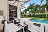 Covered patio featuring a ceiling fan, sliding glass doors, concrete decking, and a swimming pool set within a fenced yard with mature palms