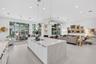 Large kitchen island with a stone-finish waterfall countertop, integrated cooktop, white shaker-style cabinetry, matte black hardware, and three glass