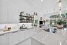 Kitchen featuring white shaker-style cabinetry, a large central island with a solid surface countertop, matte black hardware, under-cabinet lighting, 