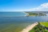 Aerial perspective featuring a direct coastal shoreline, expansive open water, a paved jetty, and manicured green space
