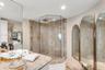 Walk-in corner shower with glass enclosure and stone-tiled surround, stone-topped vanity, and arched wall-mounted mirrors