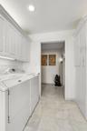Laundry area featuring white shaker-style wall cabinetry, stone-finish tile flooring, and recessed ceiling lighting