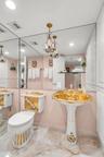 Bathroom featuring a floor-to-ceiling mirror, pedestal sink with gold-tone accents and floral detailing, matching commode, and polished stone flooring