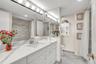 Bathroom featuring a white vanity with stone-patterned countertop, integrated basin, full-width mirror, multi-bulb light fixture, and stone-tiled show