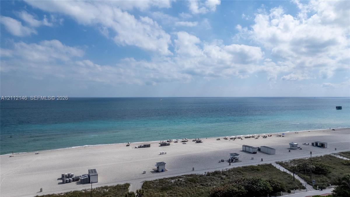 Coastal panorama featuring expansive sandy beach, turquoise ocean waters, and horizon line under a blue sky