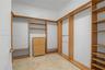 Walk-in closet featuring custom wood-finish shelving, multiple hanging rods, a built-in five-drawer dresser, and stone tile flooring