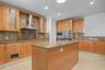 Kitchen featuring natural wood cabinetry, stone countertops, a stainless steel chimney-style range hood, integrated wall ovens, and stone tile floorin