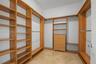 Walk-in closet featuring extensive custom wood-finish shelving, integrated hanging rods, a built-in five-drawer dresser, and stone-tile flooring