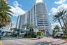 High-rise residential tower featuring a curved white facade, continuous glass-railed balconies, and a paved gated entrance