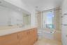 Bathroom featuring a light wood-finish vanity, stone-surfaced countertop, oversized wall mirror, tile flooring, and a combined tub and shower enclosur