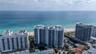 High-rise residential building featuring expansive floor-to-ceiling windows, wrap-around balconies, and direct proximity to the coastline and sandy be
