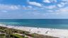 Oceanfront perspective featuring a white sand beach, turquoise water, mature palm trees, and a paved coastal pathway