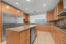 Kitchen featuring wood cabinetry, stone countertops, stainless steel full-size refrigerator, integrated beverage refrigerator, and stainless steel ran
