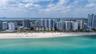 Aerial perspective of coastal property featuring direct oceanfront access, white sand beach, and dense urban skyline