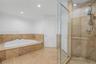 Soaking tub with a natural stone tile surround, glass-enclosed shower, polished metal fixtures, and stone tile flooring