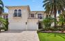 Two-story stucco exterior featuring arched windows, wrought-iron balconies, a tile roof, and a multi-car garage with paver driveway