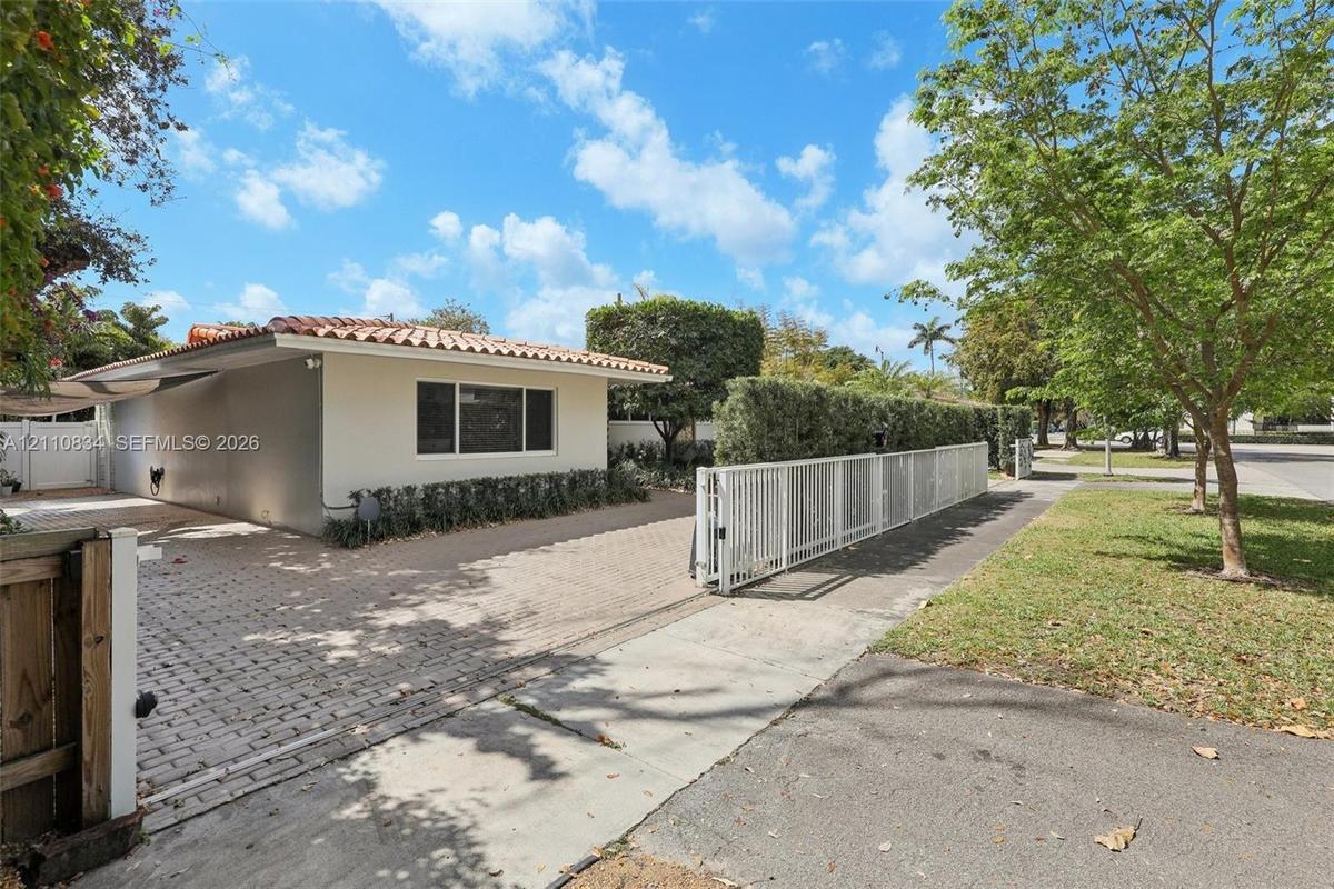 Single-story exterior featuring a clay tile roof, paved driveway, and perimeter white metal fencing
