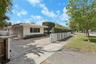 Single-story exterior featuring a clay tile roof, paved driveway, and perimeter white metal fencing