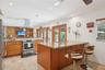 Kitchen featuring wood cabinetry, stone countertops, a center island with an integrated sink, stainless steel appliances, and stone-tile flooring