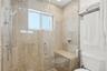 Walk-in shower enclosure featuring floor-to-ceiling stone-tile surround, built-in stone bench, glass door, and wall-mounted adjustable shower head