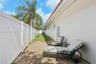 Side exterior featuring stucco siding, clay tile roof eaves, white vinyl privacy fencing, and a gravel ground cover