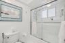Bathroom featuring white tile wall surround, glass-enclosed shower-tub combination, chrome plumbing fixtures, and a recessed ceiling light