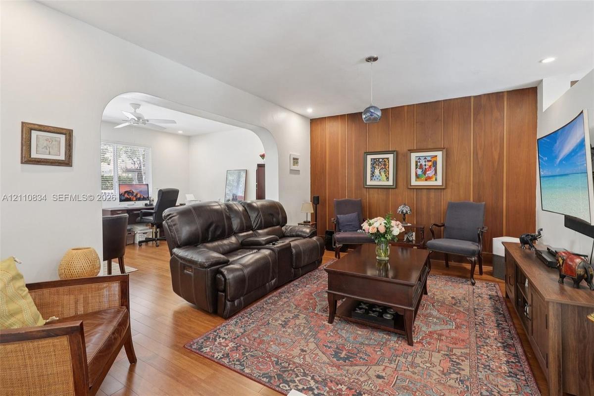 Living area featuring wood-finish flooring, a wood-paneled accent wall, a distinctive arched architectural opening, and recessed lighting