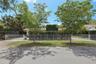 White metal perimeter fencing, gated driveway access, mature landscaping, and established trees