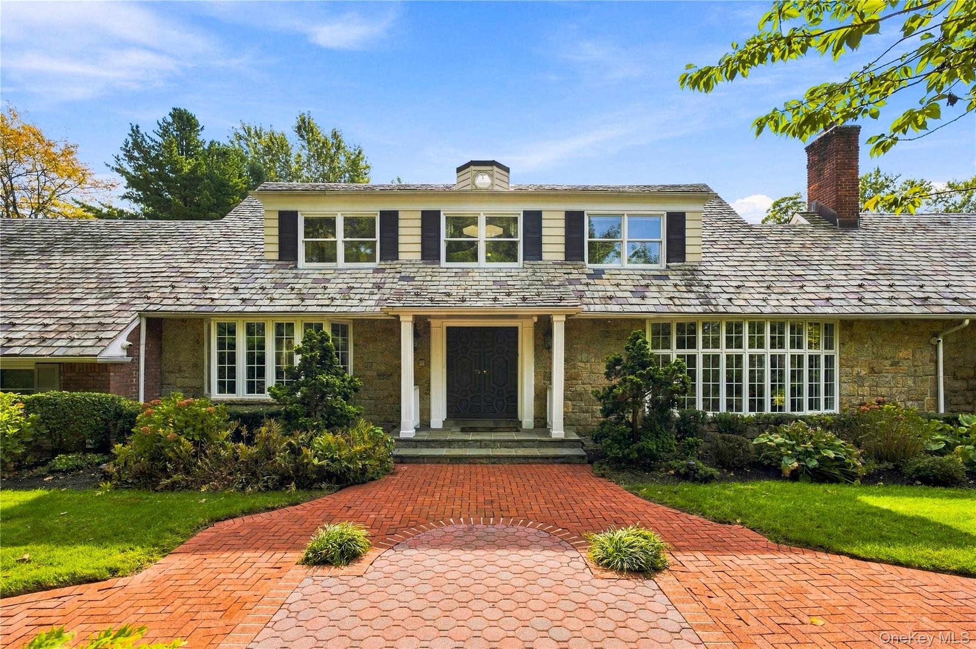 Stone and clapboard exterior featuring a covered entryway with columns, a shingled roof with a chimney, and a multi-patterned brick walkway